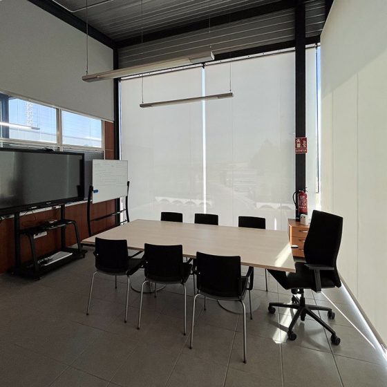 Sala de juntas con estores manuales Bandalux a medida. Monitor, mesa de juntas, sillón de dirección y sillas
