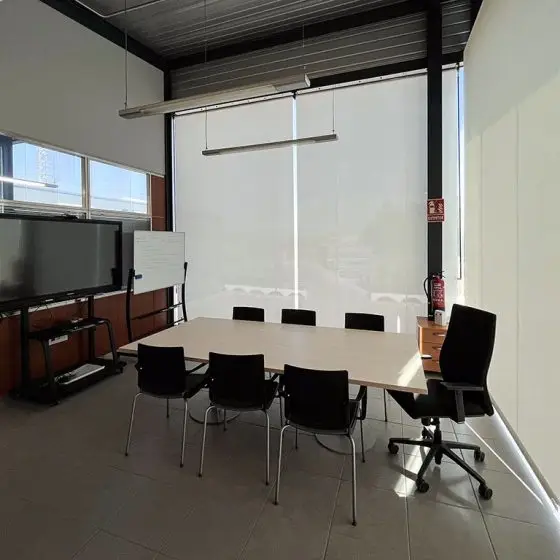 Sala de juntas con estores manuales Bandalux a medida. Monitor, mesa de juntas, sillón de dirección y sillas
